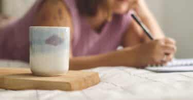 a woman writing on a notepad next to a coffee mug