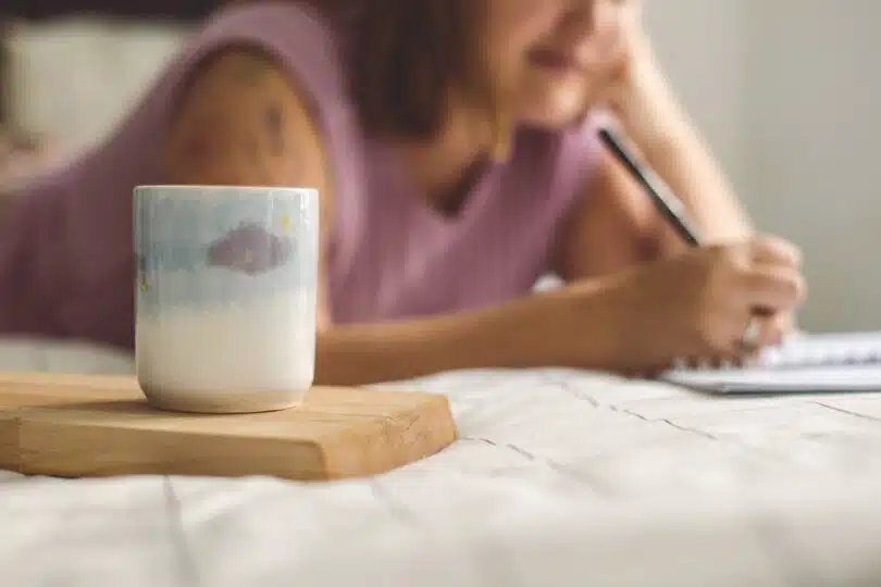 a woman writing on a notepad next to a coffee mug